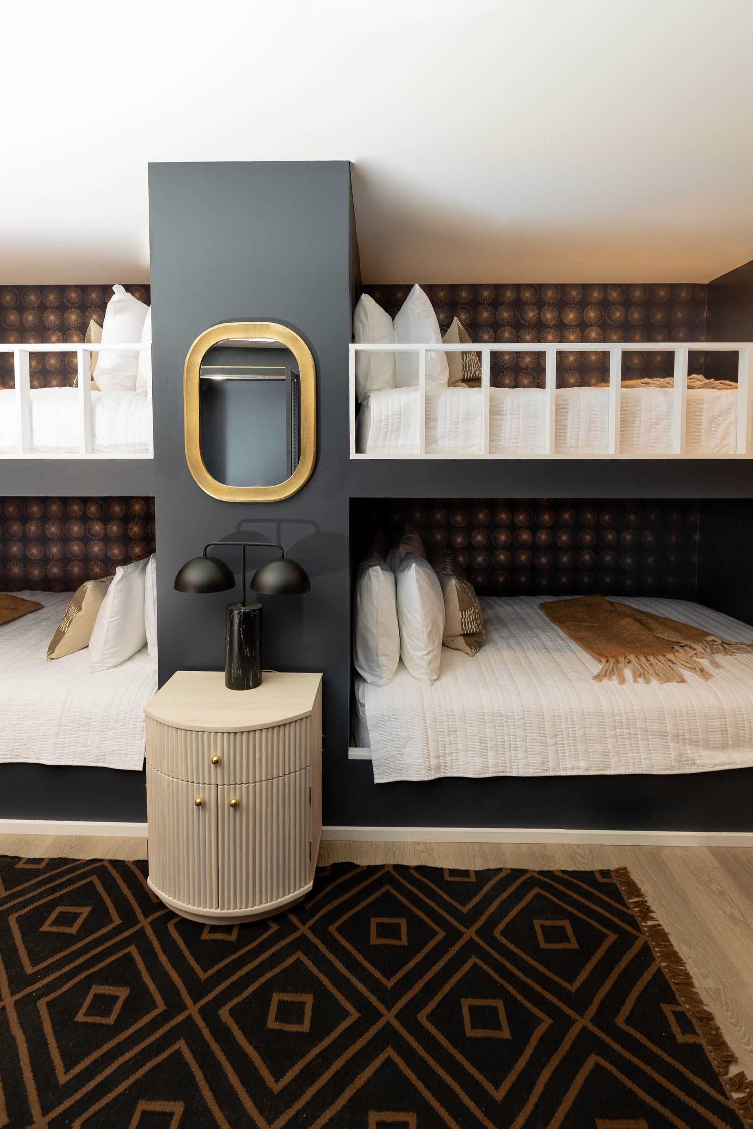 Navy queen built in bunk room design, patterened wallpaper along the back wall of the bunks, layered bedding, mirror and nightstand moment between the bunks tying it all together.