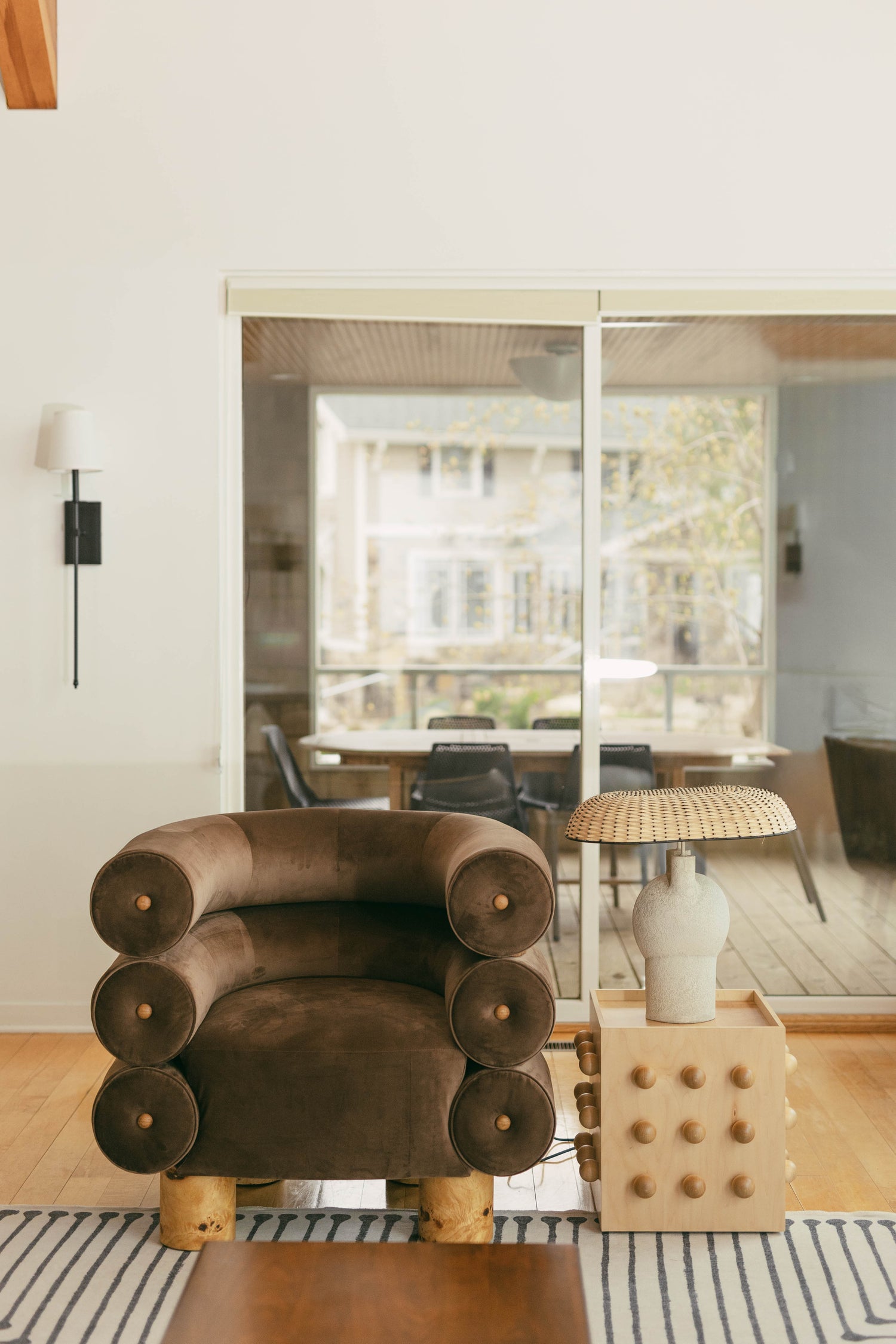 Modern living room with a brown armchair, wooden side table, and large windows.
