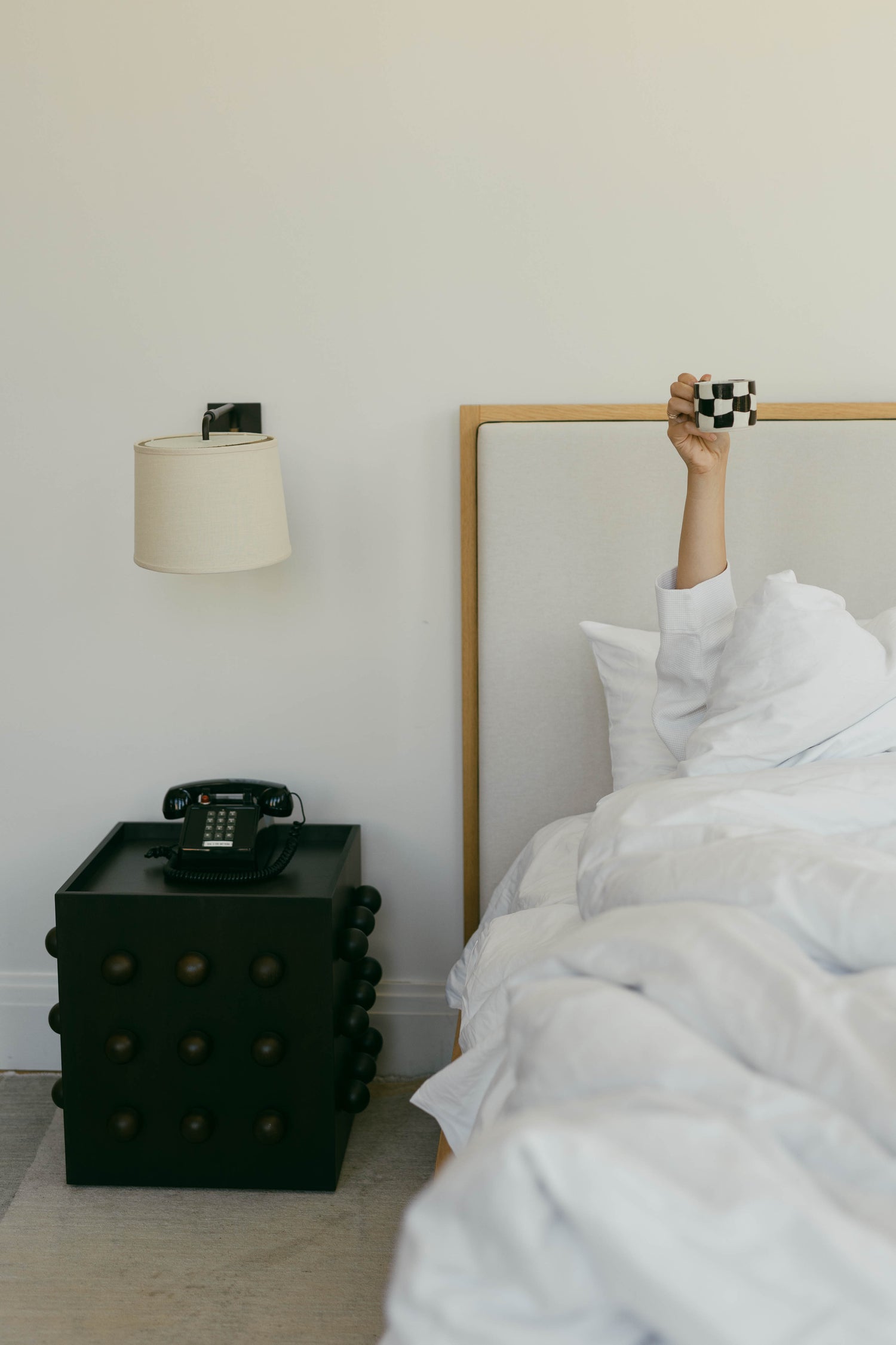 Bedroom with a bed and sculptural nightstand featuring a lamp and phone.