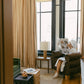 Living room with large windows, chocolate brown armchair, and person reading a newspaper with layered coffee table.
