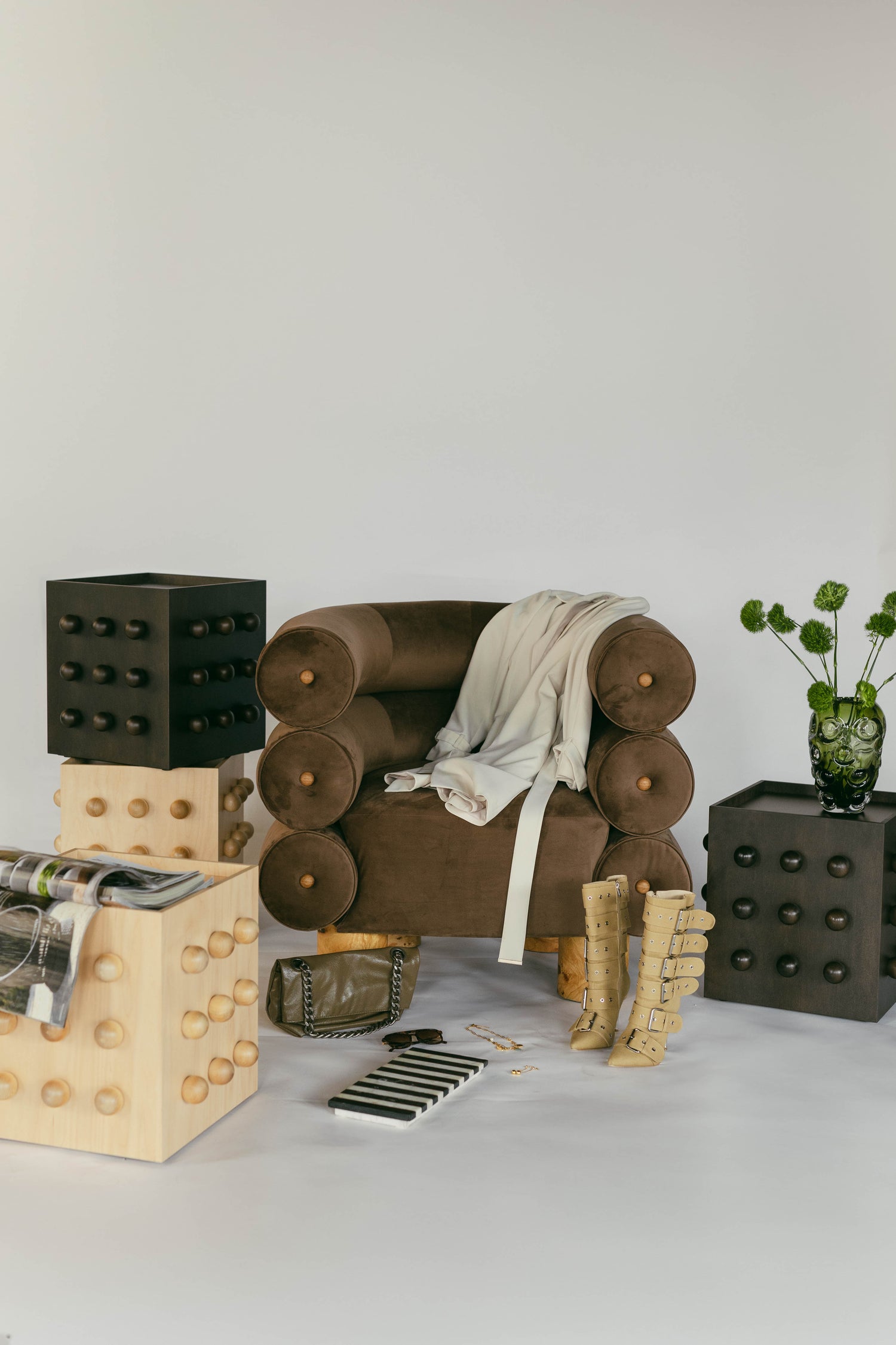 Contract Grade, Heirloom Quality furniture. Large velvet arm chair. Accent tables with 3 rows of 3 spheres styled in a studio with accessories like trench coat buckeled tall boots, vase with flowers.