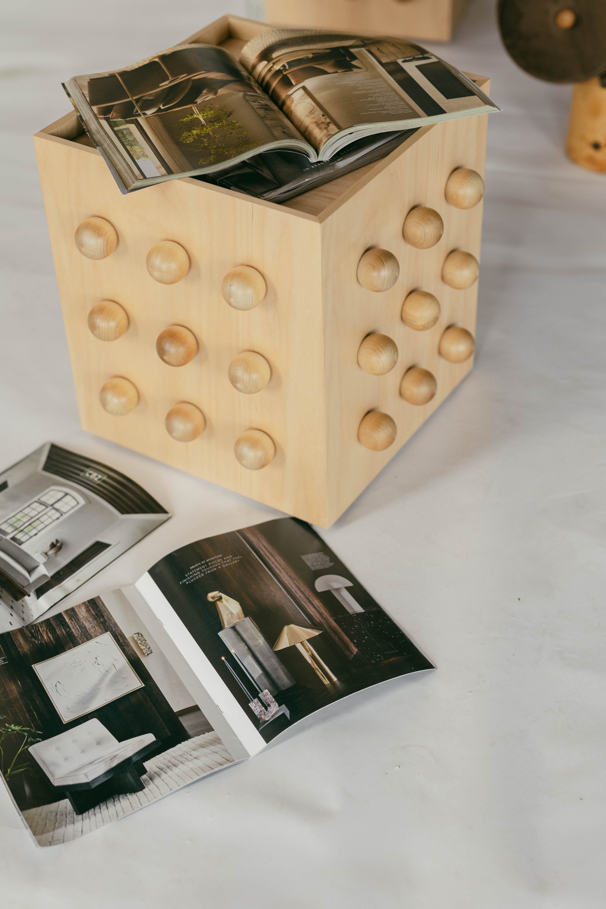 Wooden sculptural accent table with open magazines on a white surface