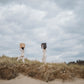 Two people carrying sculptural accent tables on beach under a cloudy sky