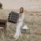 Woman holding a large deep brown accent table with protruding spheres in a desert-like setting