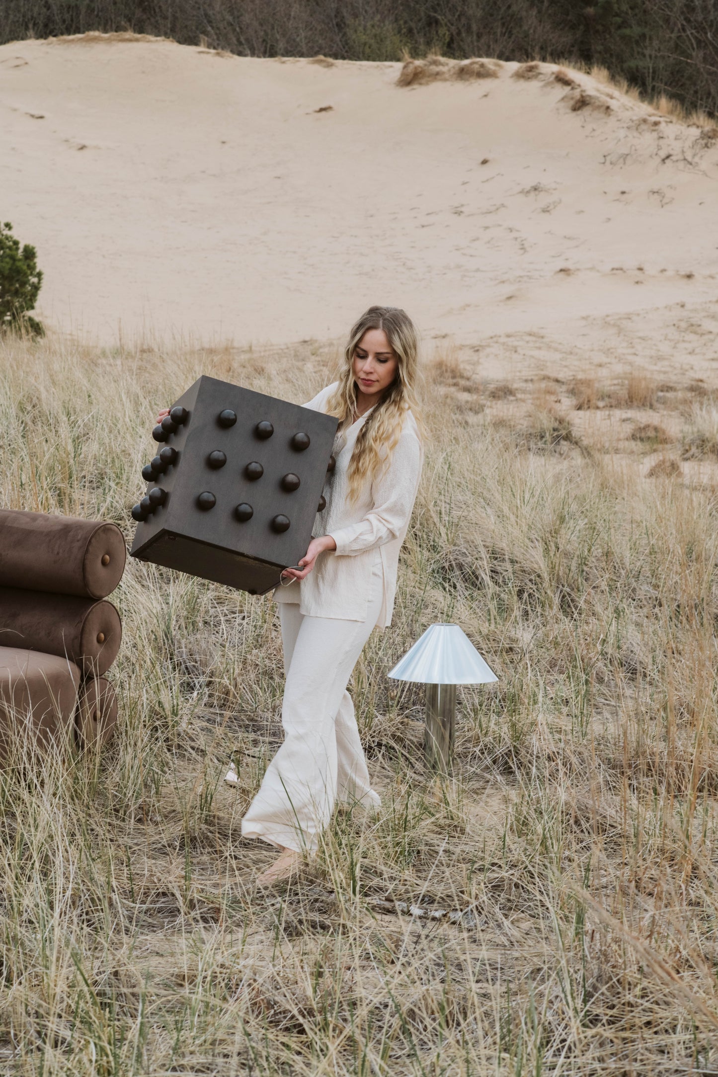 Woman holding a large deep brown accent table with protruding spheres in a desert-like setting