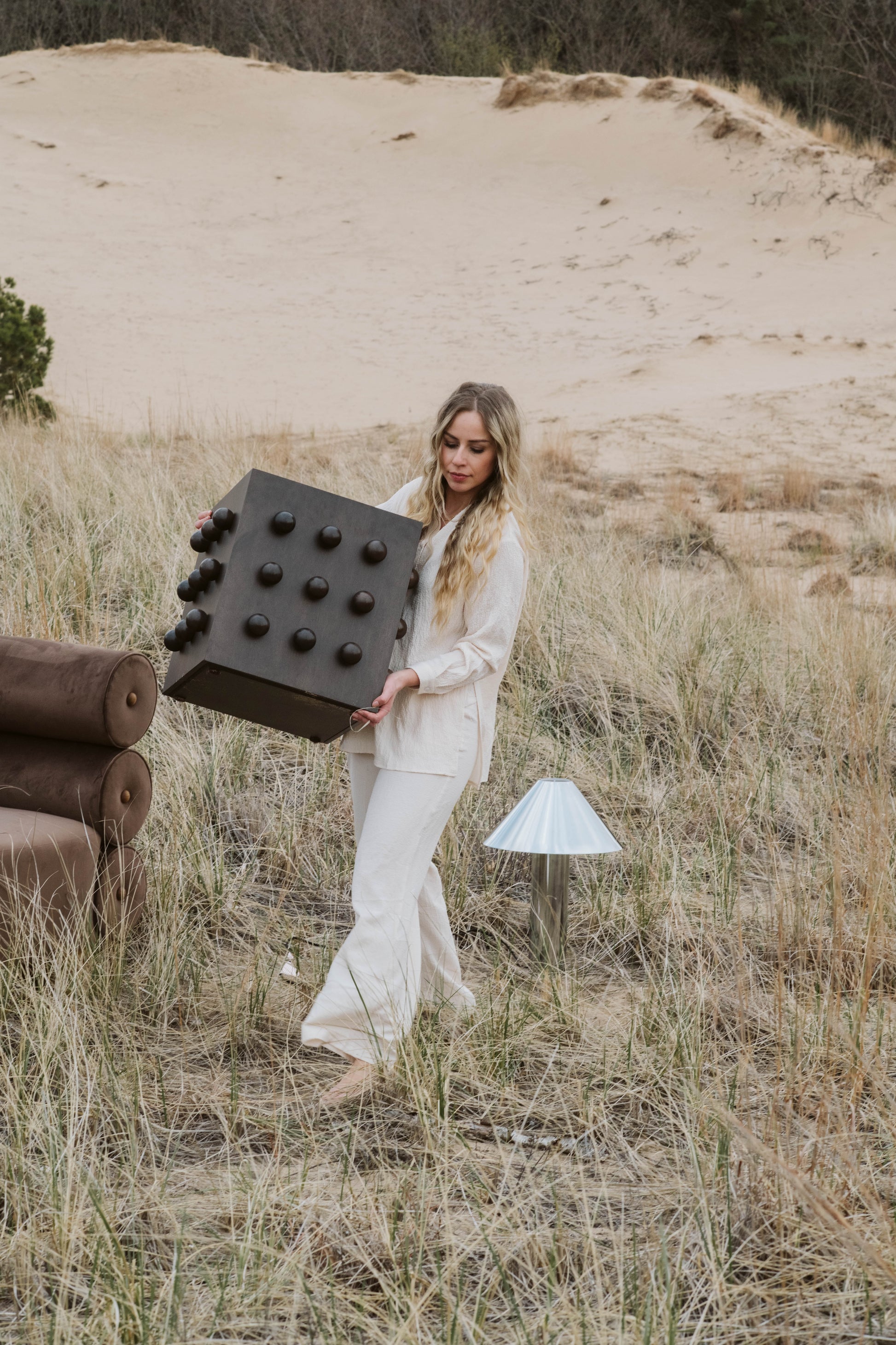Woman holding a large deep brown accent table with protruding spheres in a desert-like setting