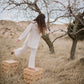 Person in a white outfit standing on wooden accent tables in a desert landscape with trees.