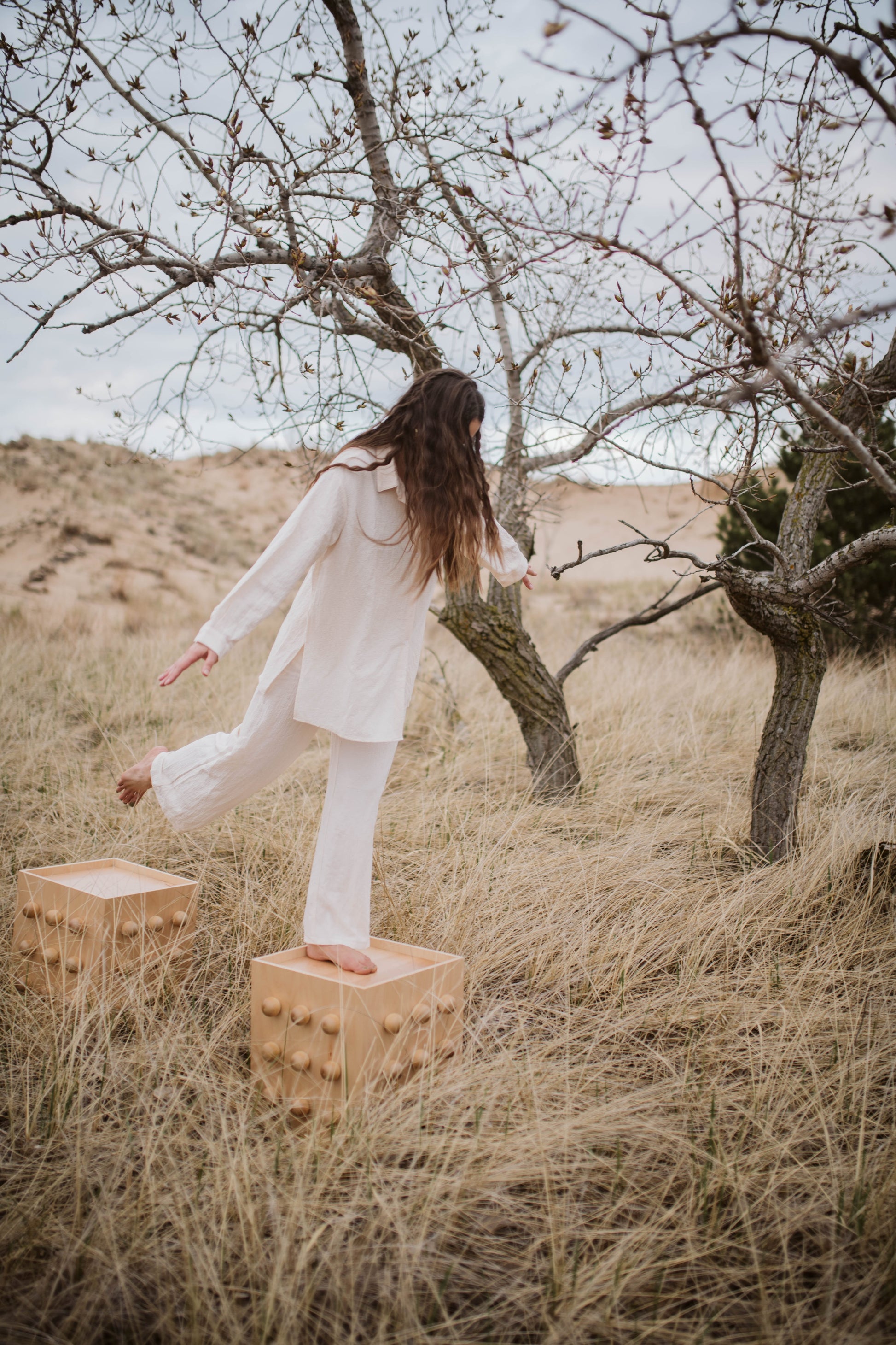 Person in a white outfit standing on wooden accent tables in a desert landscape with trees.