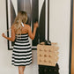 Woman in a black and white striped dress standing next to a geometric art piece on a wall.
