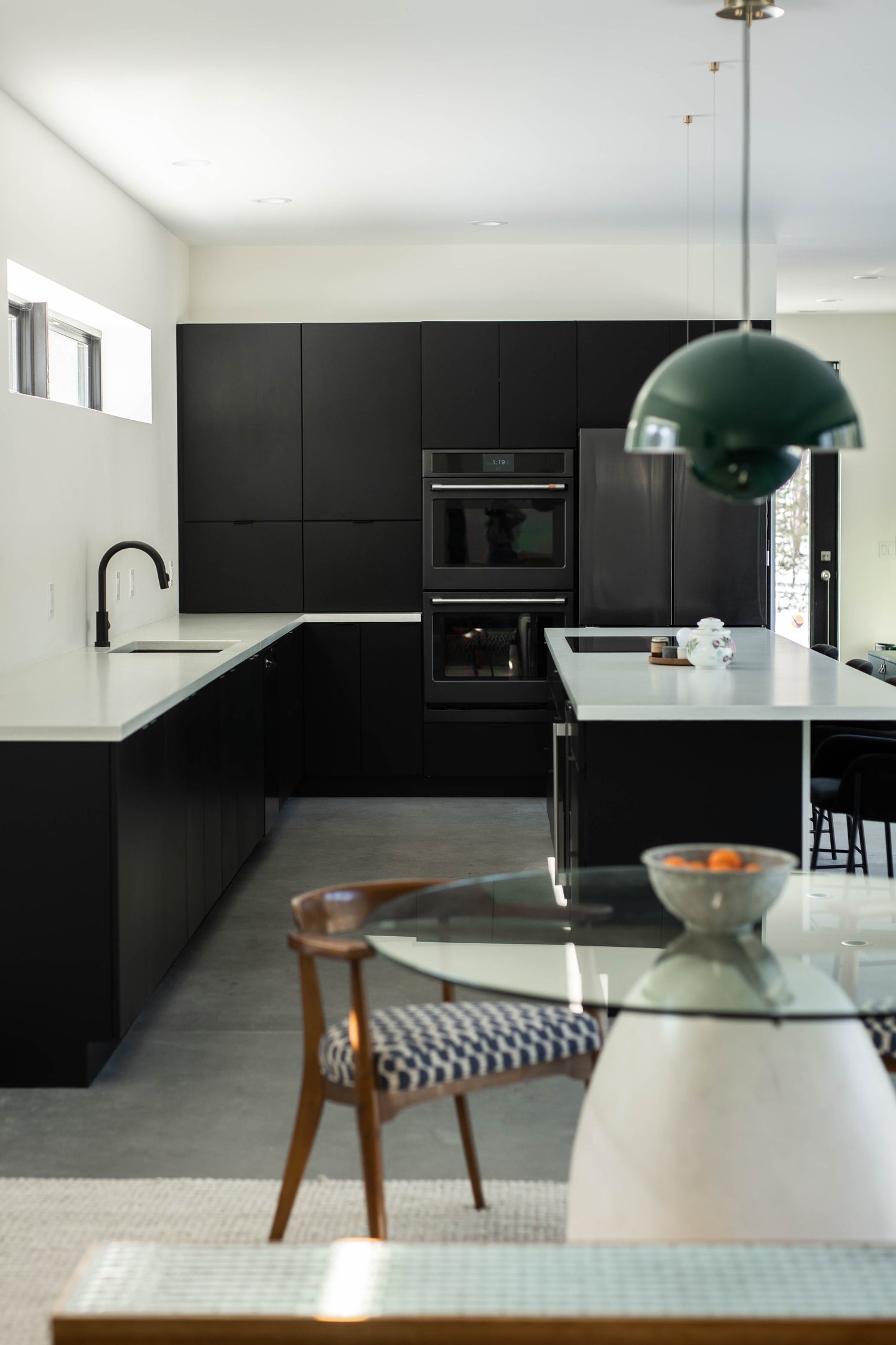 Black slab cabinets in a sleek kitchen design, glass round dinnig table, green mid century modern pendant above. 